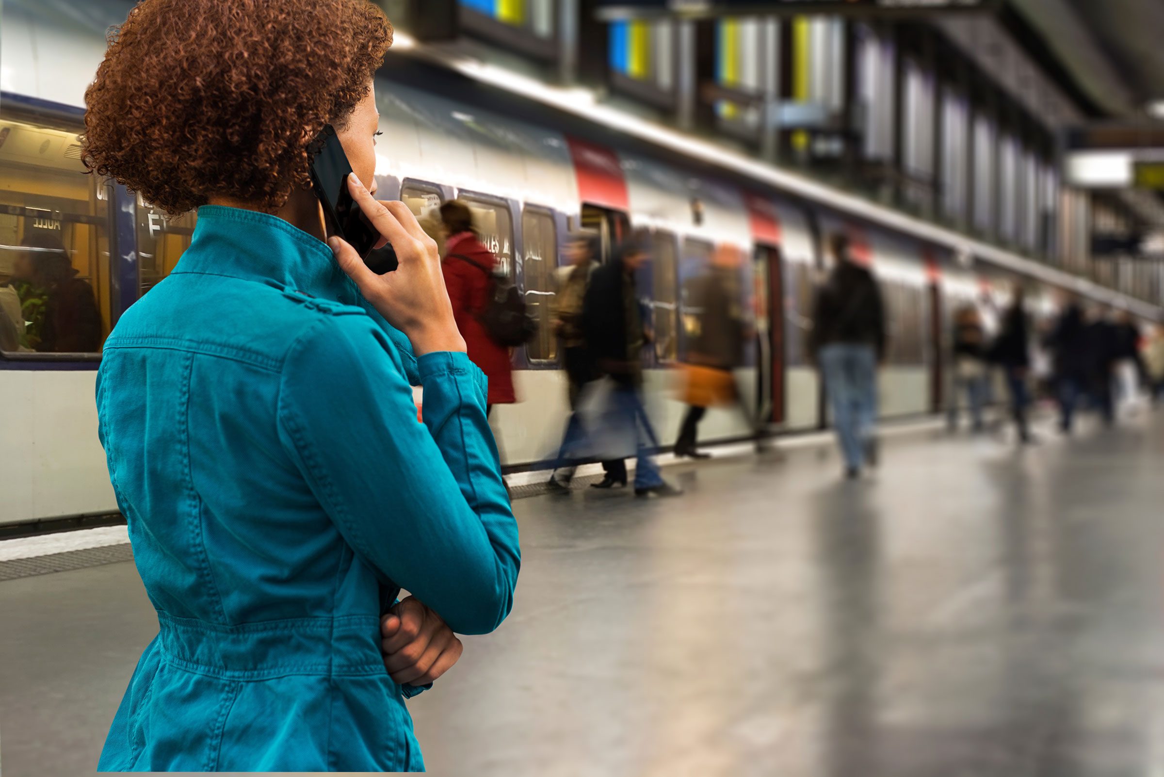 Woman on cell phone in front of a subway train.