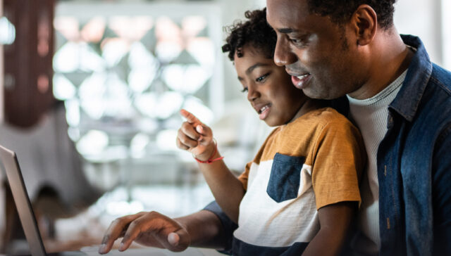 Man with child on his lap works on laptop