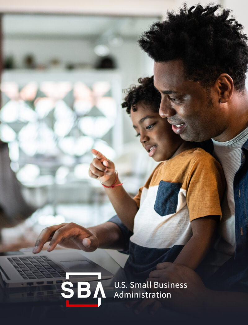 Man with child on his lap works on laptop