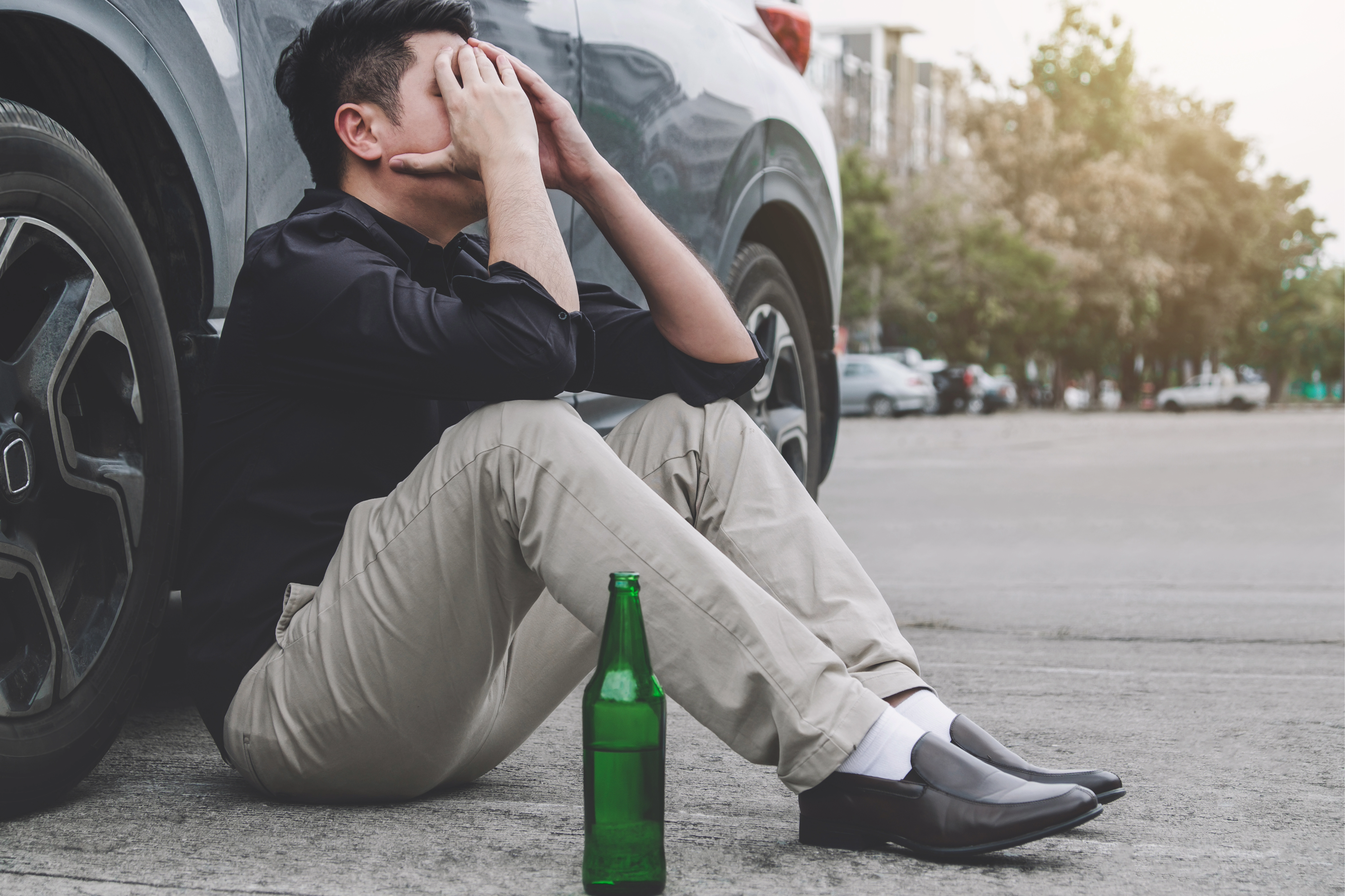 A person sitting outside of their car unable to drive because of alcohol. 