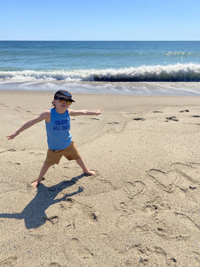 Child posing on the beach next to hearts written in the sand. 