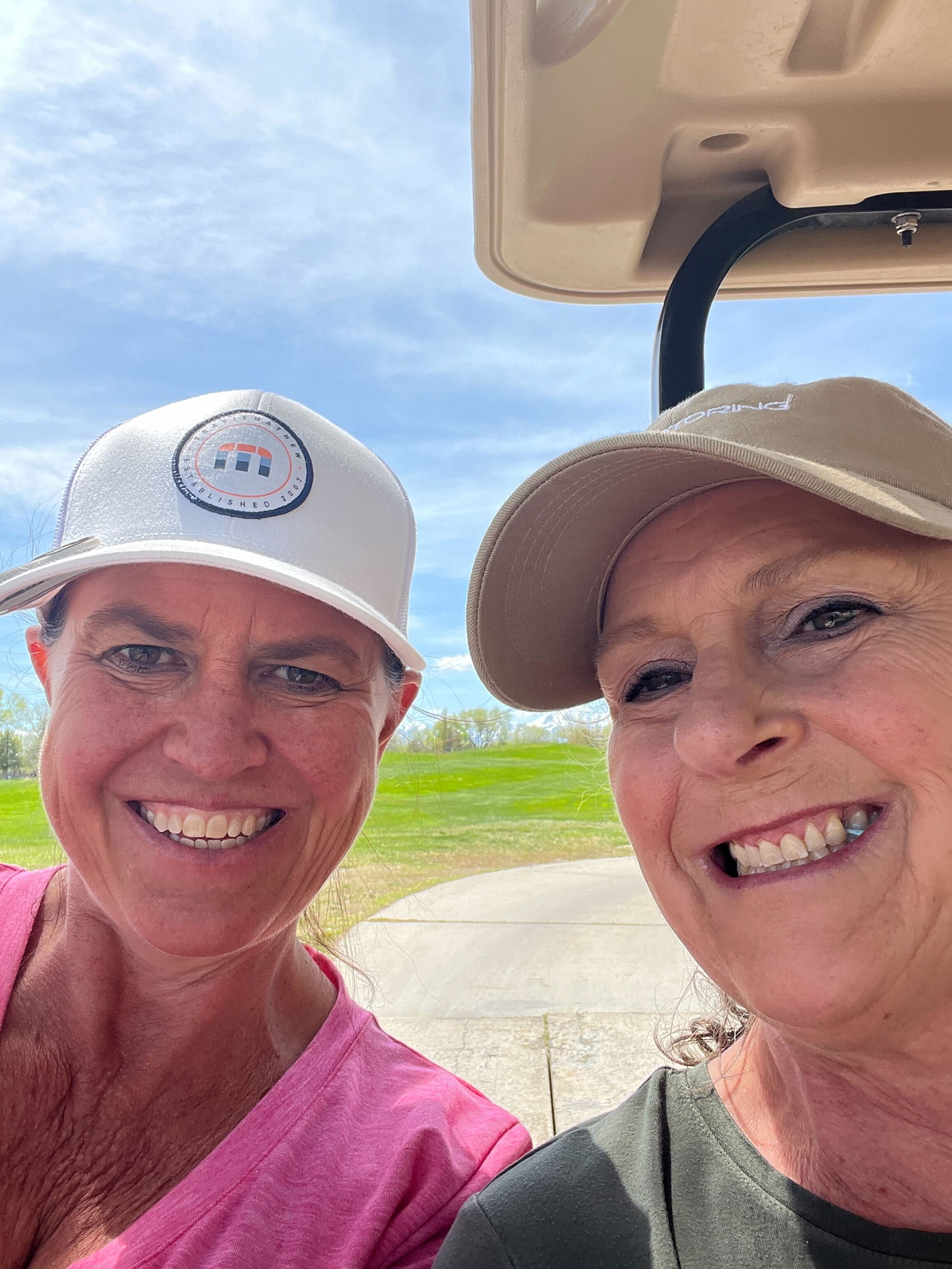Two women smiling while riding in a golf cart. 